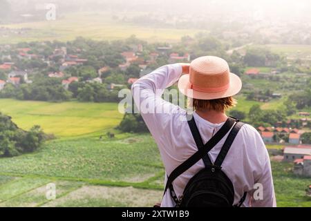 Junge Reisende, die das Dorf während des Sonnenuntergangs vom Berg aus betrachtet. Rückansicht von jungen Frauen, die in das Dorf hinunterschauen. Reisefoto, Stockfoto