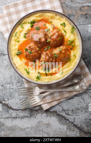 Fleischbällchen mit scharfer Sauce und einer Beilage aus Maisbrei in einer Schüssel auf dem Tisch. Vertikale Draufsicht von oben Stockfoto