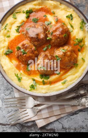 Maispolenta mit Sahne und Käse serviert mit Fleischbällchen in scharfer Soße in einer Schüssel auf dem Tisch. Vertikale Draufsicht von oben Stockfoto