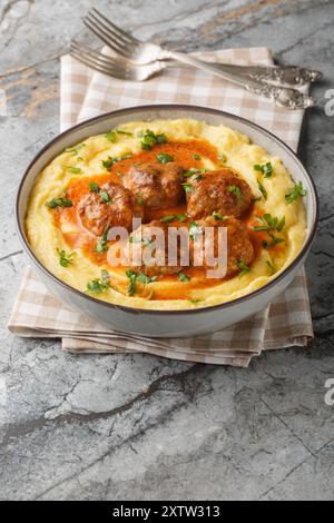 Fleischbällchen mit scharfer Sauce und einer Beilage aus Maisbrei in einer Schüssel auf dem Tisch. Vertikal Stockfoto