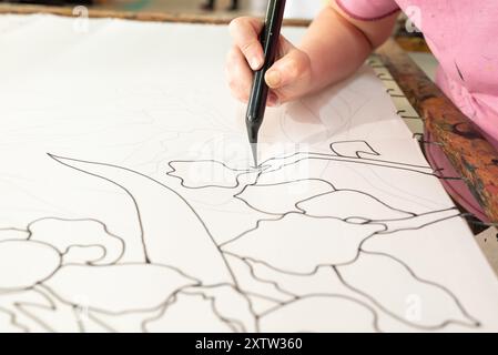 Ein erfahrener Künstler skizziert sorgfältig komplizierte Blumenmuster mit einem schwarzen Marker auf einer weißen Leinwand, die Kreativität und Handwerkskunst zum Ausdruck bringt Stockfoto