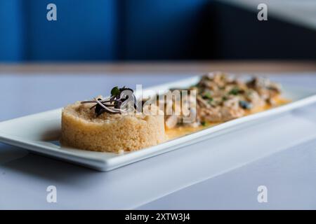 Couscous-Brei mit Fleisch- und Pilzsauce auf einer weißen Keramikplatte Stockfoto