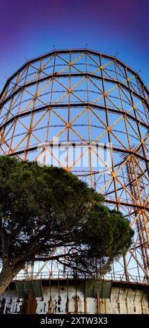 Industriekunst in Rom. Näherer Blick auf den Gazzometro am Abend, mit dunkelblauem Himmel im Hintergrund. Stockfoto