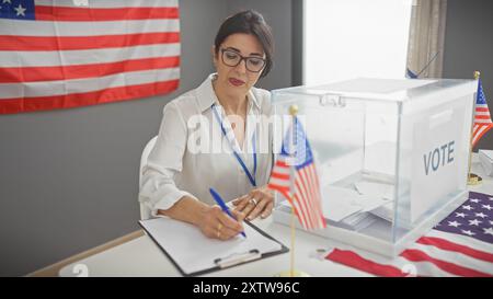 Eine reife hispanische Frau überwacht die Abstimmung in einem mit amerikanischen Fahnen geschmückten Raum. Stockfoto