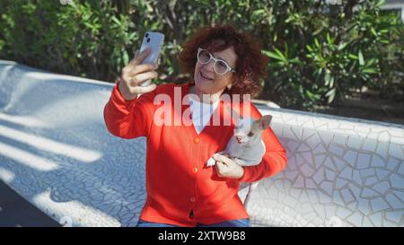 Eine ältere Frau in einem roten Pullover macht ein Selfie mit ihrem chihuahua an einem sonnigen Tag in einem Stadtpark. Stockfoto