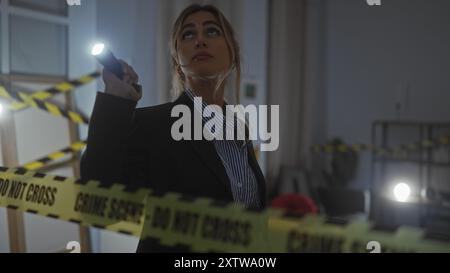 Eine junge blonde Frau untersucht einen Tatort drinnen, beleuchtet von ihrer Taschenlampe. Stockfoto