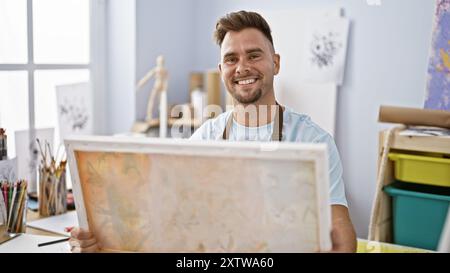 Ein lächelnder Künstler, der Leinwand in einem hellen Kreativstudio hält. Stockfoto