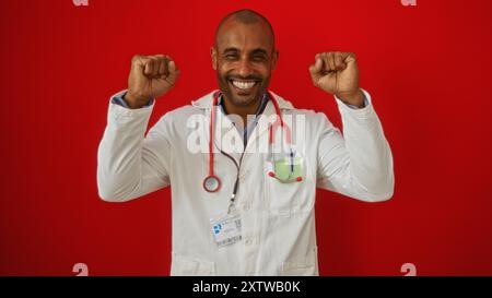 Hübscher Doktor Mann über isoliertem rotem Hintergrund, der fröhlich mit geballten Fäusten lächelt und den Erfolg mit weißem Mantel und Stethoskop feiert Stockfoto