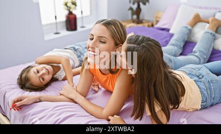 Eine lächelnde Frau genießt eine schöne Zeit drinnen mit ihren beiden Töchtern in einem gemütlichen Schlafzimmer. Stockfoto