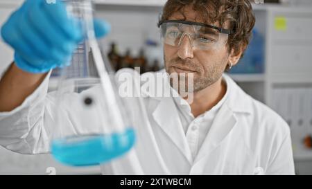 Ein professionell aussehender Mann mit Bart untersucht eine Flasche mit blauer Flüssigkeit in einem modernen Labor. Stockfoto