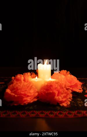 Drei Kerzen brennen hell, umgeben von Ringelblumen auf dunklem Hintergrund. Die Tischdecke Day of the Dead verleiht dieser vertikalen Tischdecke eine authentische Note Stockfoto