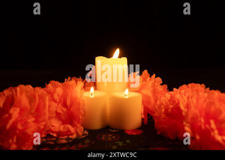 Vertikale Aufnahme mit drei beleuchteten Kerzen in der Mitte, umgeben von leuchtenden orangefarbenen Ringelblumen. Die Szene, die nur von Kerzenlicht beleuchtet wird, ruht auf Stockfoto