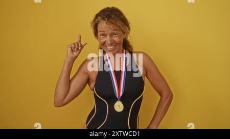 Ältere Frau trägt Medaille isoliert an der gelben Wand, lächelt und gestickt, während sie im Badeanzug gekleidet ist, und zeigt Stolz und Freude an ihrem Akcompli Stockfoto