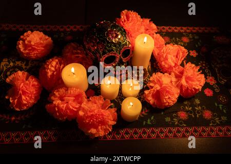 Blick von oben auf einen dekorierten Schädel mit metallischen Blumen, umgeben von leuchtenden orangefarbenen Ringelblumenblättern. Zündete Kerzen und ein Tag der Toten Muster Stockfoto