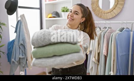 Lächelnde hispanische Frau, die Kleidung in einem modernen Kleiderschrank hält. Stockfoto