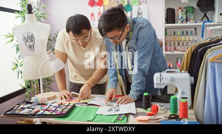 Zwei Männer arbeiten in einem bunten Schneideratelier zusammen, umgeben von Stoffen, Fäden und Entwurfsskizzen. Stockfoto