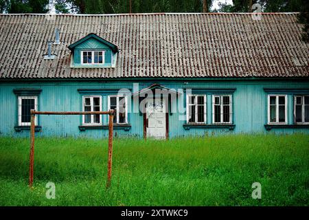 Verlassenes rustikales Haus mit bewachsenem Gras und rostiger Schaukel in ländlicher Gegend Stockfoto