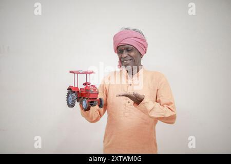 Indischer Bauer, der Mini-Traktorspielzeug für Kredite und Bankgeschäfte hält, Erfolg eines armen und alten Bauers Stockfoto