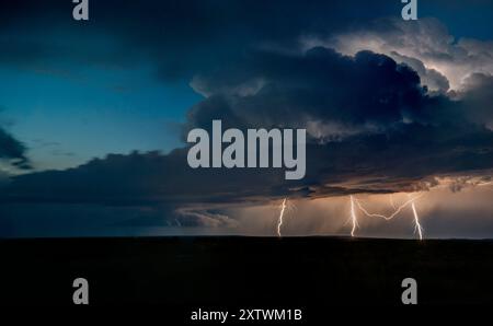 Blitze erleuchten den dunklen stürmischen Himmel über einer ruhigen Ebene in der Abenddämmerung. Stockfoto