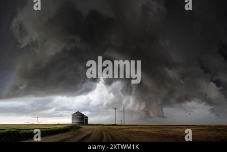 Unheilvolle Sturmwolken erheben sich über einer Landstraße mit einem einsamen Gebäude und einem Telefonmast, was auf ein bevorstehendes Unwetterereignis hindeutet. Stockfoto