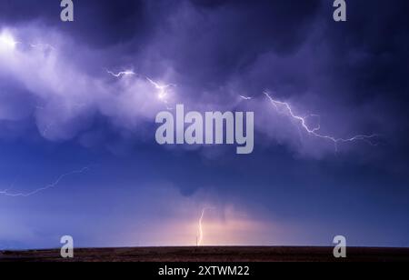 Blitze erleuchten den Nachthimmel über einer flachen Landschaft. Stockfoto