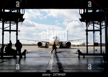 Silhouettenfiguren arbeiten um ein Flugzeug in einem Hangar herum, mit klarem Himmel im Hintergrund. Stockfoto