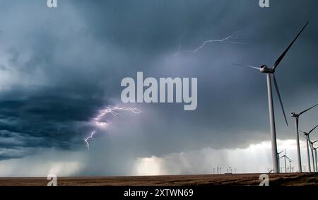 Dunkle Gewitterwolken schweben über einem Windpark mit Blitzen in der Ferne und zeigen ein dramatisches Wetterereignis über Turbinen mit erneuerbarer Energie. Stockfoto