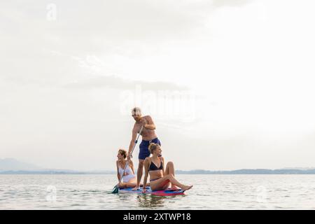 Gruppe von Freunden, die bei Sonnenuntergang auf einem ruhigen See paddeln. Stockfoto