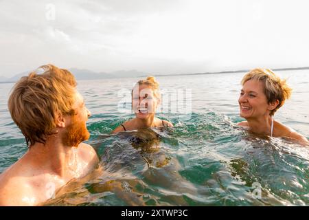 Drei Personen schwimmen gerne im Meer und lachen zusammen an einem sonnigen Tag. Stockfoto
