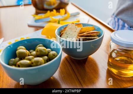 Eine Auswahl an Snacks auf einem Holztisch mit Crackern, Käse, grünen Oliven und Honig in einem Glas. Stockfoto