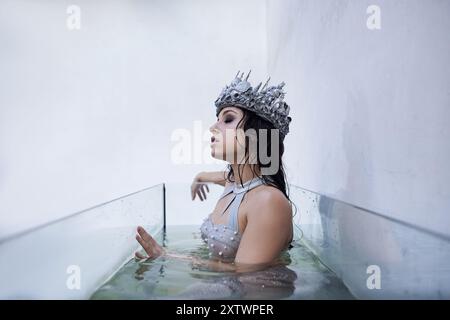 Eine junge Frau mit einer Krone, mit Silber geschmückt, schwimmt in einem modernen Aquarium. Stockfoto