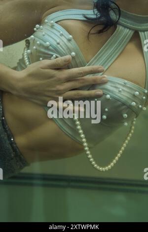 Eine Meerjungfrau mit fließenden brünetten Haaren und einem perlfarbenen Mieder gleitet anmutig durch das Wasser. Stockfoto