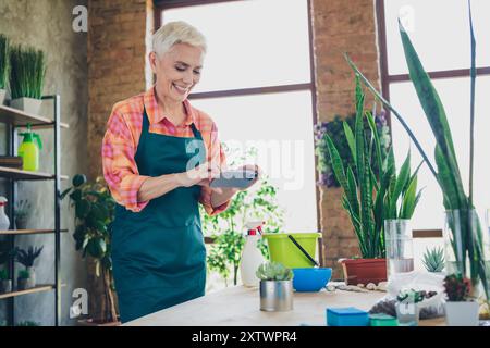 Foto der glänzenden glücklichen Age Frau gekleidet Schürze Aufnahme Video Pflanzen moderne Gadget Indoor Home Werkstatt Stockfoto