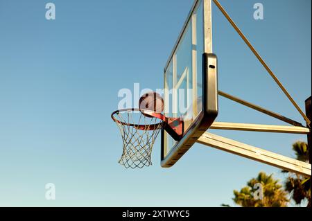 Basketballkorb im Freien mit einem Ball, der durch das Netz gegen einen klaren blauen Himmel geht. Stockfoto