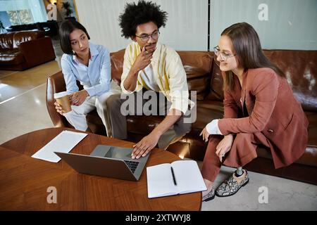 Drei Kollegen treffen sich in einer modernen Bürolobby und diskutieren Ideen, während sie ein Notebook und ein Notebook verwenden. Stockfoto