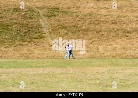 Zwei Frauen laufen durch einen Landpark, eine hält ihr Handy hoch, um Fotos zu machen. August 2024. Stockfoto