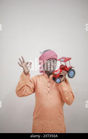 Indischer Bauer, der Mini-Traktorspielzeug für Kredite und Bankgeschäfte hält, Erfolg eines armen und alten Bauers Stockfoto