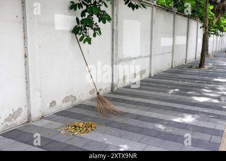 Ein Besen lehnt sich an die Wand, Besen und Laub, Besenstiele stehen allein. Stockfoto