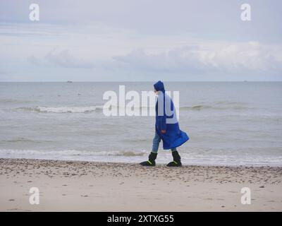 Ein Mann mit blauem Regenmantel und wasserdichten Stiefeln, der am Strand Grenen in Skagen entlang geht. Stockfoto