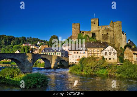 Ein malerischer Blick auf ein historisches Schloss und traditionelle Häuser entlang eines Flusses mit einer Steinbrücke unter einem klaren blauen Himmel in Deutschland. Stockfoto