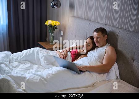 Ein Paar, das sich umarmt, sieht sich etwas auf dem Laptop an Stockfoto