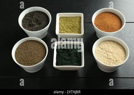 Verschiedene Superfood-Pulver in Schüsseln auf schwarzem Holztisch Stockfoto