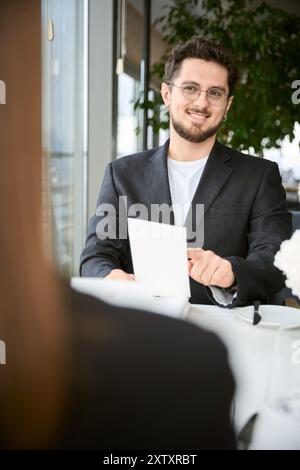 Glücklicher bärtiger Mann in Gläsern mit Menü, der Frau im Restaurant ansieht Stockfoto