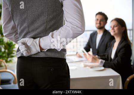 Der Kellner hält seine Hand hinter seinem Rücken, während er eine Bestellung von einem jungen Paar entgegennimmt Stockfoto