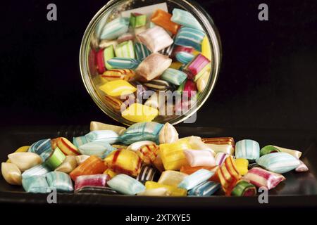 Bunte harte Bonbons in einem Glas und auf einem schwarzen Tablett auf schwarzem Hintergrund Stockfoto