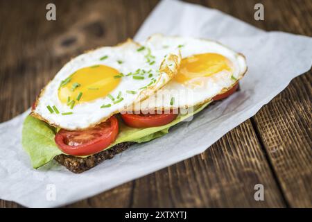 Frisch zubereitetes gebratenes Ei-Sandwich (detaillierte Nahaufnahme, selektiver Fokus) auf einem Holztisch Stockfoto