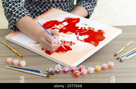 Die Hand einer Frau zeichnet ein Gemälde mit einem Pinsel und Farben Stockfoto