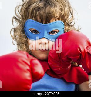 Superheldenkind mit Boxhandschuhen vor blauem Himmel. Mädchenmacht und Feminismuskonzept Stockfoto