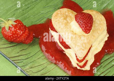 Herzförmige Erdbeeren und Vanillefeuille auf Erdbeersauce, auf grünem Hintergrund. Für einen süßen Valentinstag. Selektiver Fokus Stockfoto