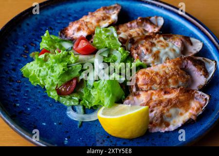 Fisch Und Meeresfrüchte. Muschelmuscheln. Gebackene Muscheln mit Käse, Koriander und Zitrone in Schalen auf gusseiserner schwarzer Platte. Teller mit Muscheln, kaltem Weißwein, Zitrone Stockfoto